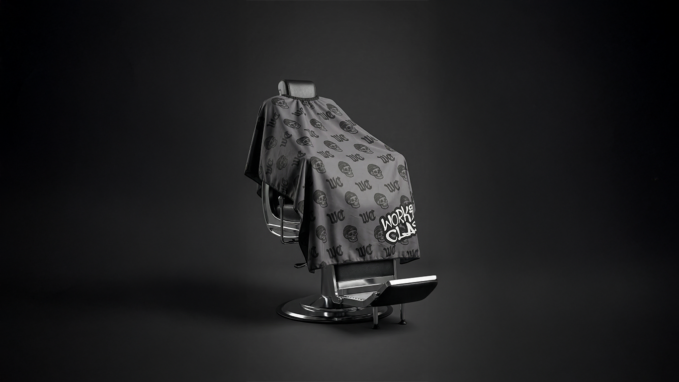Monogram barber cape draped over a salon chair, featuring dual-closure neck system and durable fabric for professional hairdressing use.
